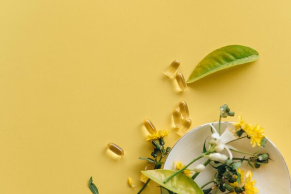 Flat lay of herbal supplements, flowers, and leaves on a bright yellow background.